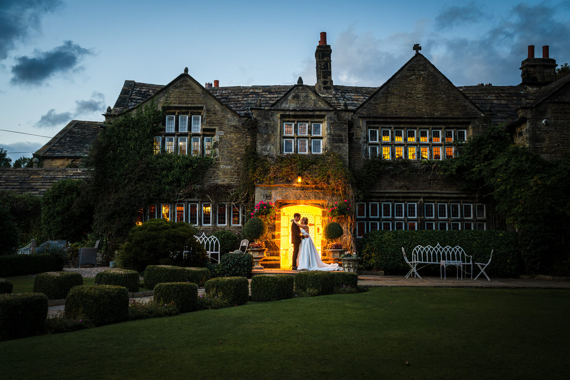 Romantic hero shot of bride and groom at dusk embracing outside holdworth house white door